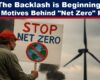 Expose News Protester holding "Stop Net Zero" sign with wind turbine in background, highlighting controversy over net-zero plans and environmental impacts.