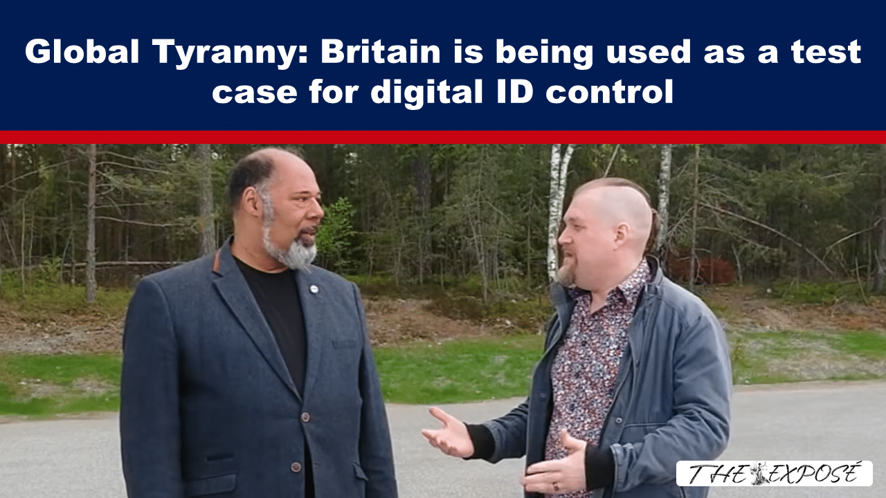 Two men standing outdoors and talking under a blue banner that reads 'Global Tyranny: Britain is being used as a test case for digital ID control'.