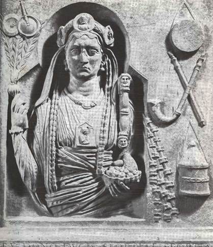 Stone relief of a regal female figure with an ornate headdress and layered necklaces, holding a small statue and ceremonial object.
