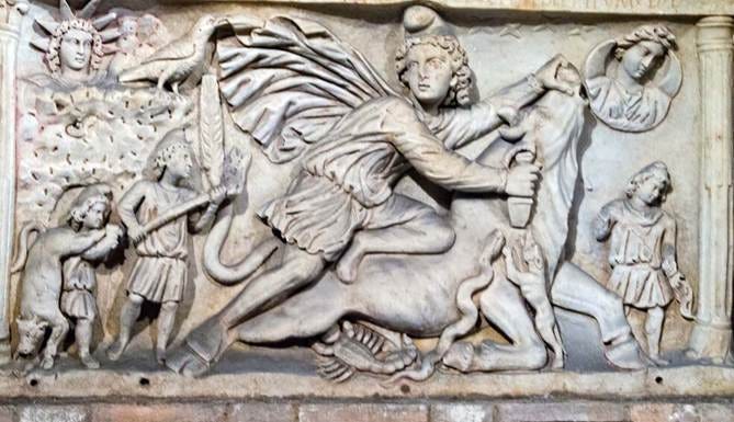Stone relief of a rider on a horse slaying a dragon, with small figures to the left and a sun motif, plus a circular medallion to the right.
