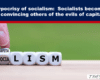 Headline about socialism hypocrisy; close‑up of a hand placing a dice block reading 'CAPITA' atop dice forming 'SOCIALISM' with a green background and The Exposé logo in corner.