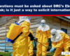 Medical workers in yellow hazmat suits disinfect an outdoor area beside a wooden building during an Ebola outbreak cleanup.