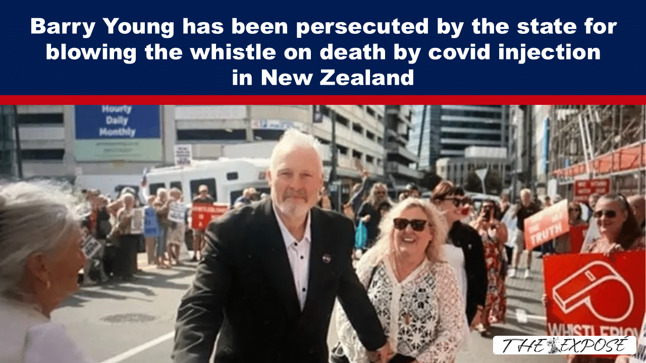 Crowd of protesters marching down a city street, led by a man in a dark suit; signs call out about Covid injections and whistleblowing in New Zealand.