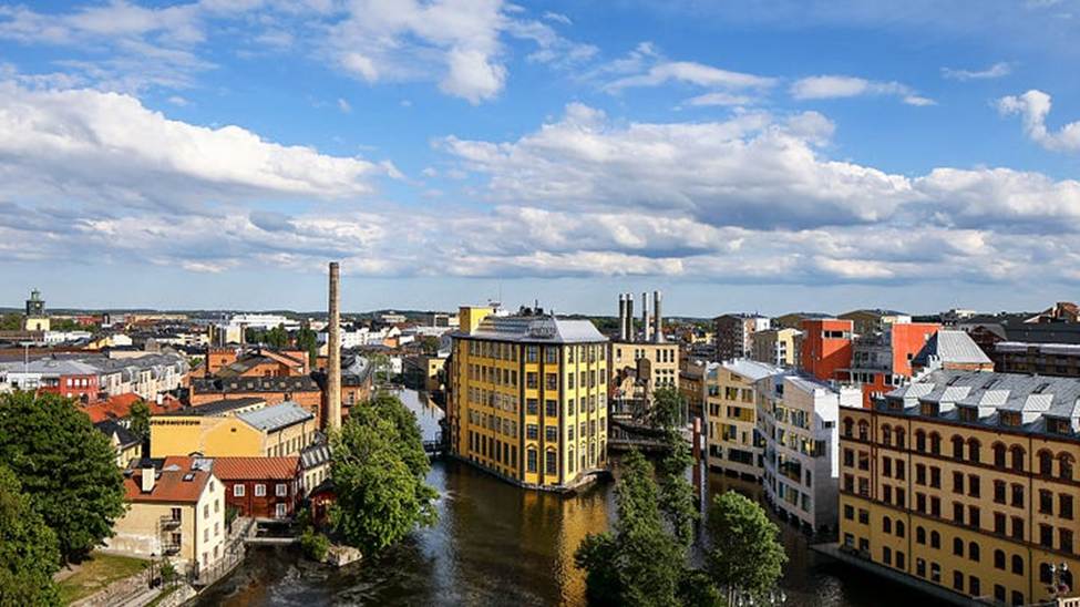 image - The Expose Aerial view of a European city with a canal and colorful buildings along the water, under a blue sky with clouds.