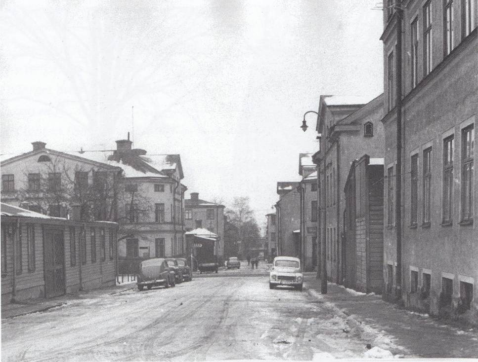image - The Expose Snowy urban street with parked cars and brick buildings on both sides, black-and-white winter scene.