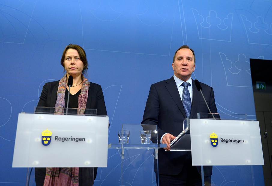 image - The Expose Two officials in business attire speak at podiums with microphones during a government briefing, against a blue backdrop with government insignia.