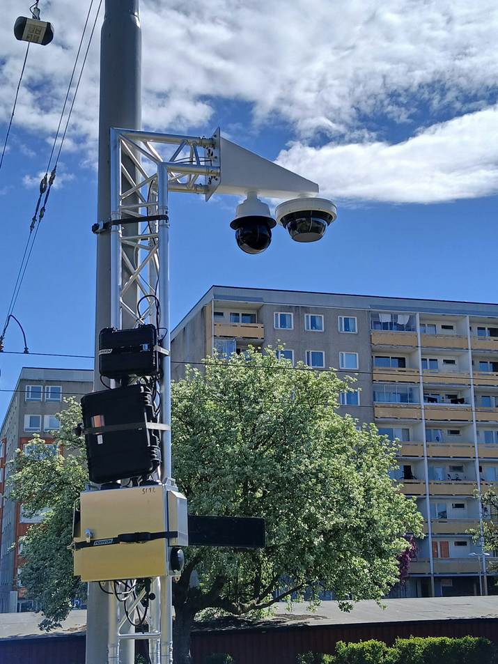 image - The Expose Traffic surveillance cameras mounted on a metal pole against a blue sky with a residential building in the background.