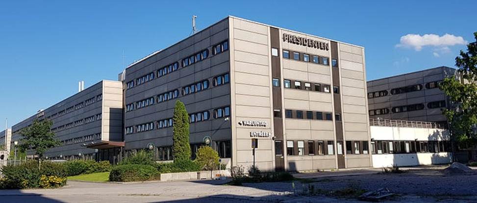 image - The Expose Large beige multi-story office building with 'PRESIDENTEN' sign, surrounded by trees and a parking area.